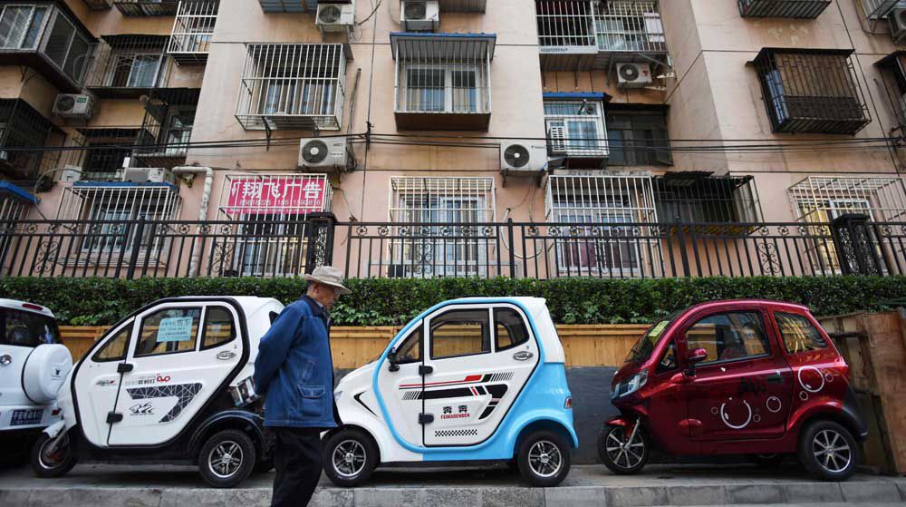  A man walks past electric cars and tricycles on a sidewalk in Beijing.