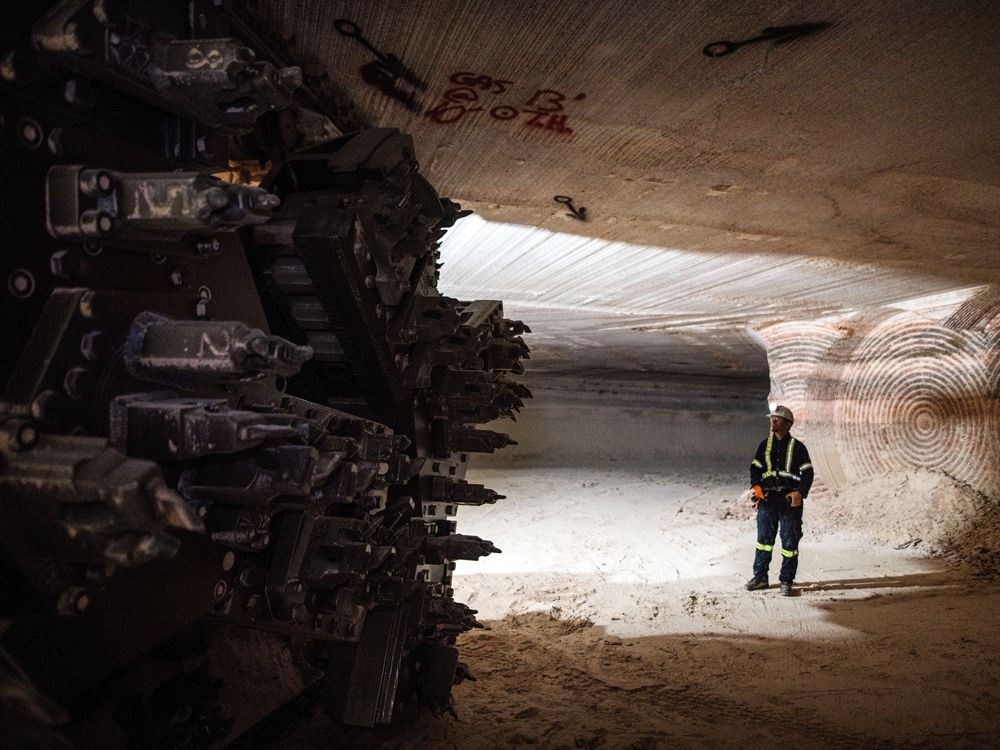  A miner stands near the cutting head of a digger near an active mining wall at the [nxtlink id=