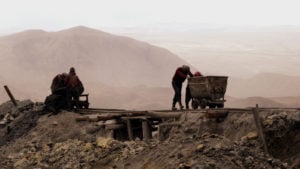 Mine workers pushing carts in mountainous region.