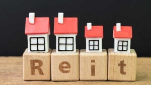 tiny house figures atop letter blocks spelling out REIT, representing reits to buy. stock predictions. undervalued reits