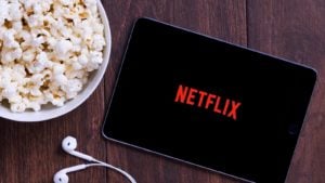 The Netflix logo on a tablet with earbuds and a bowl of popcorn nearby.