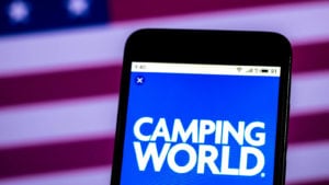 Camping World (CWH) logo on a smartphone in front of an American flag background.