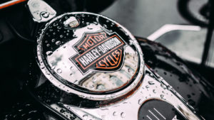 A close-up photograph of the tank to a Harley-Davidson motorcycle with raindrops on it.