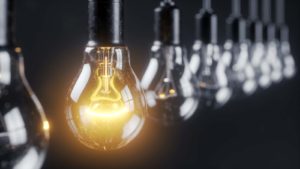 Utilities stocks: a stock image of light fixtures; one lightbulb is lit up