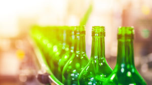 green beer bottles in a factory line, ready to be sealed. represents packaging companie