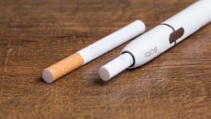 An image of a cigarette and an e-cigarette side-by-side on a wood surface.