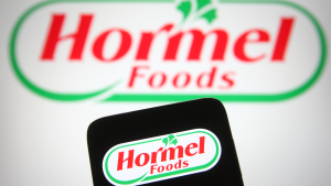 Hormel Foods Logo shown on a laptop screen behind a phone screen also showing the logo. HRL stock.