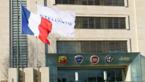A flag with the logo for Stellantis waves outside a building with the logos for some of its car brands, including Abarth, Lancia, Fiat, Alfa Romeo and Jeep.