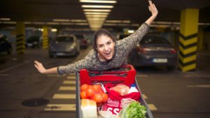 a woman with her hands splayed out as wings while running with a cart full of groceries in front of her