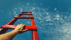 A hand reaches up on a red ladder pointing to the sky.